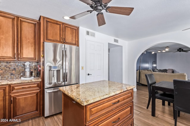 kitchen with stainless steel refrigerator with ice dispenser, decorative backsplash, light stone counters, and light wood-type flooring