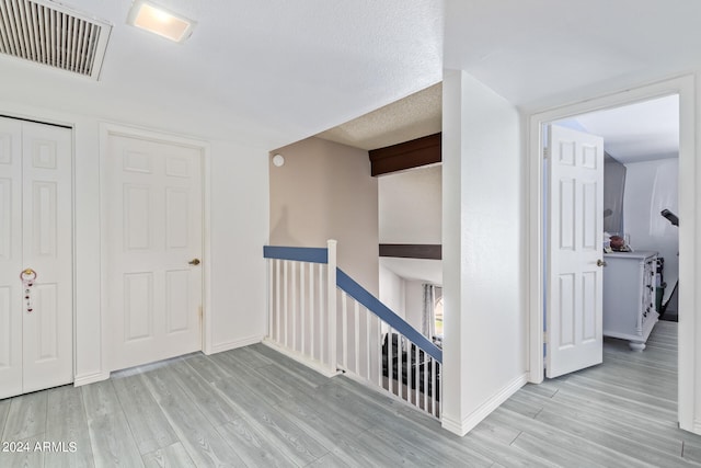 hall featuring vaulted ceiling, a textured ceiling, and light hardwood / wood-style floors