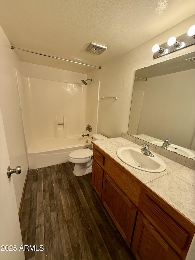 full bathroom featuring a textured ceiling, hardwood / wood-style floors, bathing tub / shower combination, vanity, and toilet