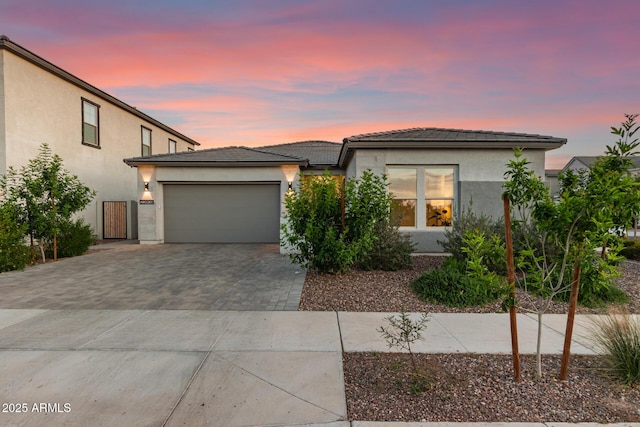 view of front of home with stucco siding, decorative driveway, a tiled roof, and an attached garage