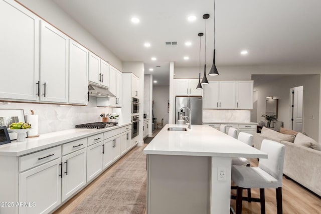 kitchen with appliances with stainless steel finishes, tasteful backsplash, a sink, recessed lighting, and light wood finished floors