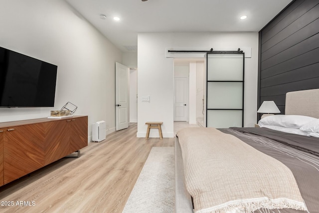bedroom with a barn door, light wood-style flooring, recessed lighting, and baseboards