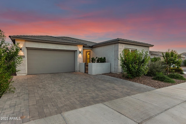 view of front facade with decorative driveway, an attached garage, stucco siding, and a tiled roof