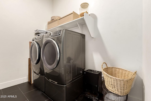 clothes washing area with washing machine and dryer, dark tile patterned flooring, and baseboards