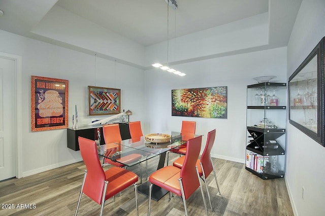 dining room with a raised ceiling, wood finished floors, and baseboards