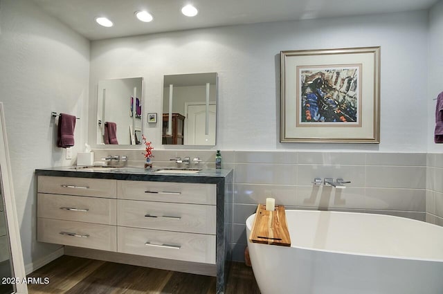 bathroom with a freestanding bath, double vanity, wood finished floors, and a sink