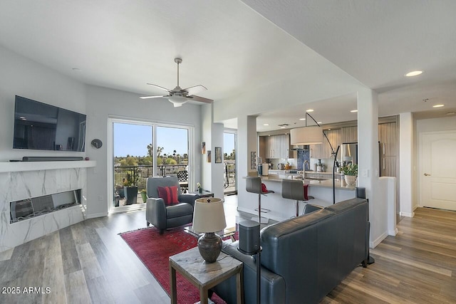 living area featuring baseboards, a fireplace, wood finished floors, and a ceiling fan