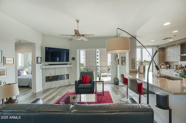 living area with a ceiling fan, baseboards, light wood finished floors, recessed lighting, and a fireplace