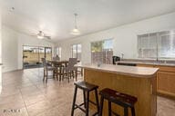 kitchen featuring ceiling fan, a center island, hanging light fixtures, a kitchen bar, and light tile patterned floors