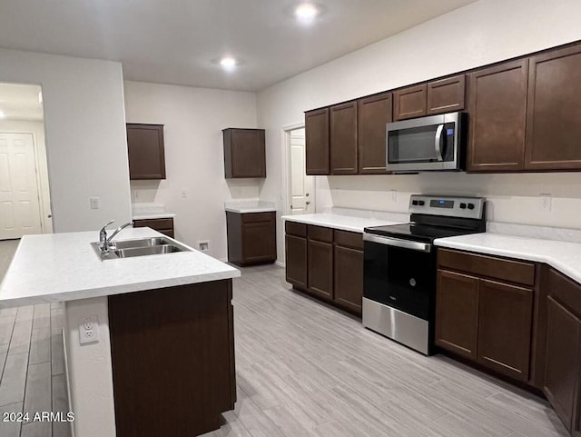 kitchen with stainless steel appliances, a kitchen island with sink, light hardwood / wood-style floors, and sink