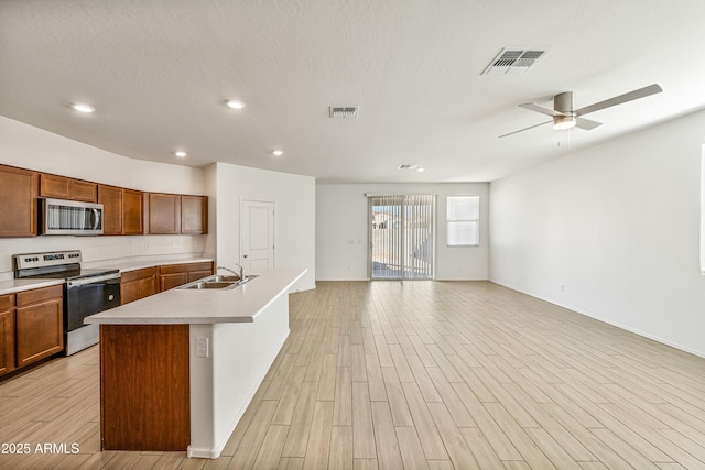 kitchen with sink, a kitchen island with sink, ceiling fan, stainless steel appliances, and light wood-type flooring