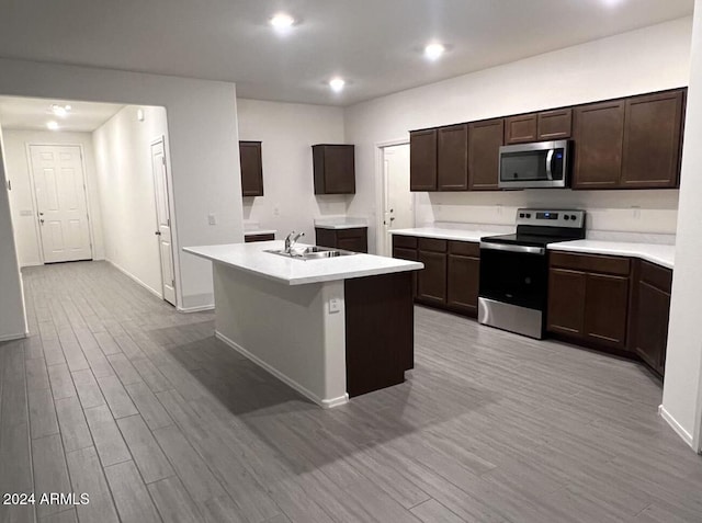 kitchen with sink, dark brown cabinets, a center island with sink, light hardwood / wood-style flooring, and stainless steel appliances