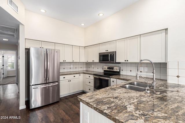 kitchen with sink, stainless steel appliances, dark stone countertops, a towering ceiling, and white cabinets