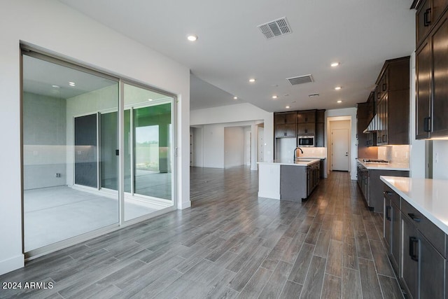 kitchen with appliances with stainless steel finishes, dark brown cabinetry, dark hardwood / wood-style floors, sink, and a kitchen island with sink