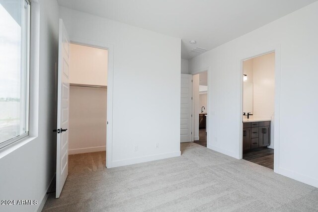 unfurnished bedroom featuring light carpet, ensuite bath, and a spacious closet