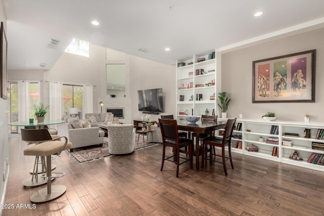 dining area featuring visible vents, a tiled fireplace, vaulted ceiling, recessed lighting, and dark wood-style flooring