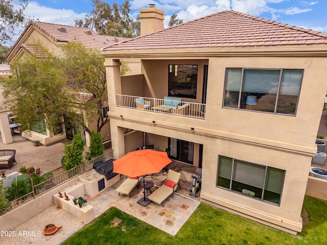 rear view of house featuring stucco siding, a balcony, a patio area, and a chimney