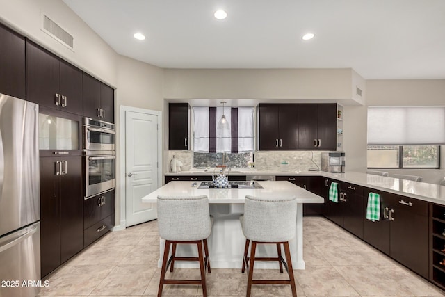 kitchen featuring visible vents, a kitchen bar, light countertops, stainless steel appliances, and open shelves