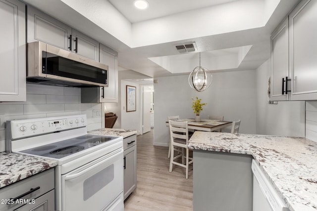 kitchen featuring a tray ceiling, backsplash, white appliances, and gray cabinetry