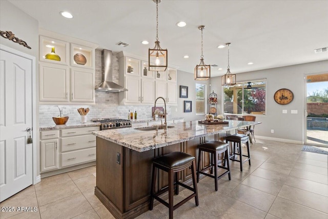 kitchen featuring hanging light fixtures, white cabinetry, a center island with sink, and wall chimney exhaust hood