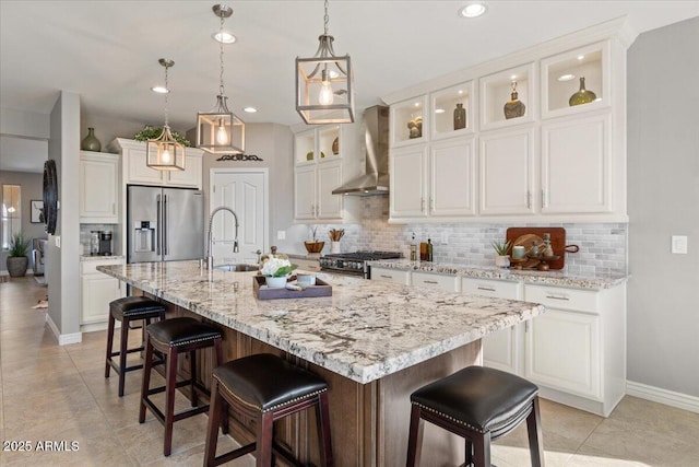 kitchen with high quality appliances, sink, white cabinets, a center island with sink, and wall chimney exhaust hood