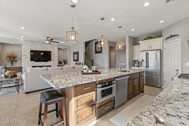 kitchen with sink, decorative light fixtures, light tile patterned floors, a large island with sink, and appliances with stainless steel finishes