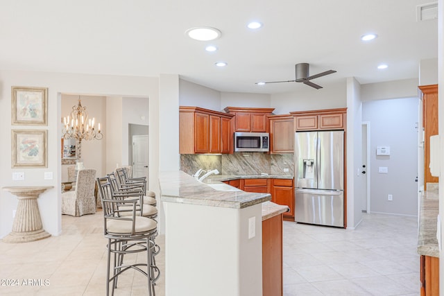 kitchen with a kitchen breakfast bar, appliances with stainless steel finishes, kitchen peninsula, backsplash, and ceiling fan with notable chandelier