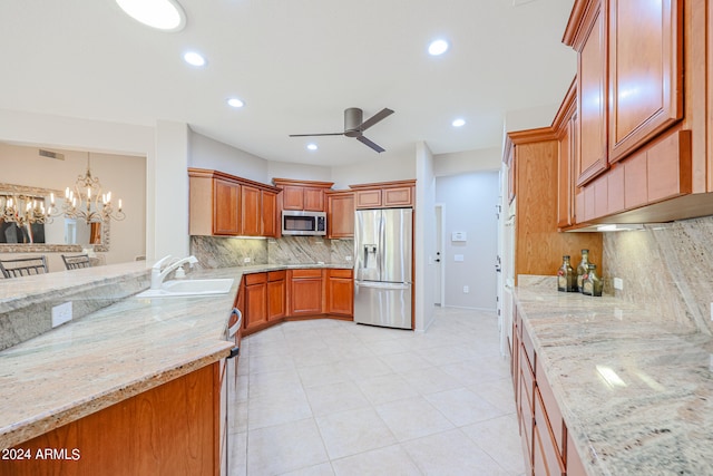 kitchen with stainless steel appliances, decorative light fixtures, tasteful backsplash, ceiling fan with notable chandelier, and light stone countertops