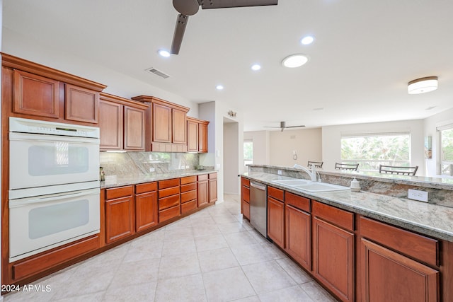 kitchen featuring double oven, ceiling fan, light stone counters, sink, and stainless steel dishwasher