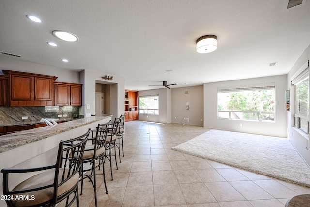 kitchen with a breakfast bar area, light stone countertops, light tile patterned floors, ceiling fan, and tasteful backsplash