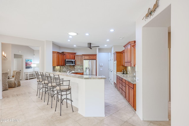 kitchen with kitchen peninsula, stainless steel appliances, tasteful backsplash, a kitchen bar, and ceiling fan