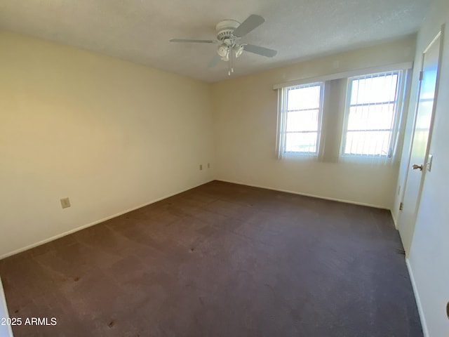 spare room with ceiling fan and dark colored carpet