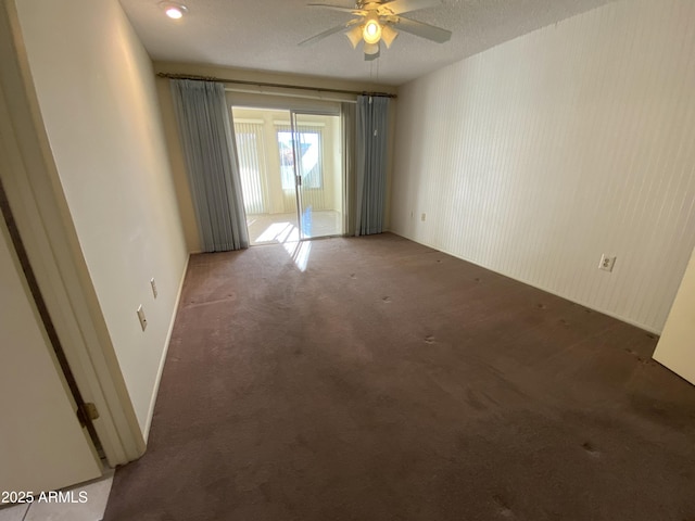 spare room featuring ceiling fan, dark carpet, and a textured ceiling