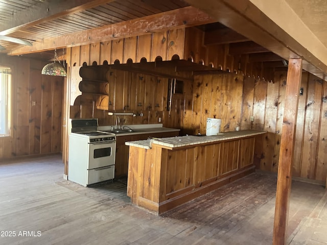 kitchen featuring gas range gas stove, kitchen peninsula, wooden walls, dark wood-type flooring, and tile counters