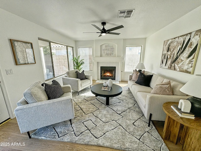 living room with visible vents, ceiling fan, a textured ceiling, wood finished floors, and a tile fireplace