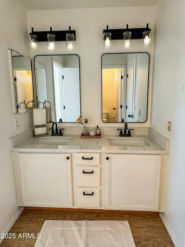 bathroom featuring double vanity, wood finished floors, a sink, and baseboards