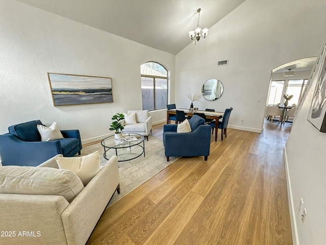 living room featuring light wood-type flooring, an inviting chandelier, plenty of natural light, and arched walkways