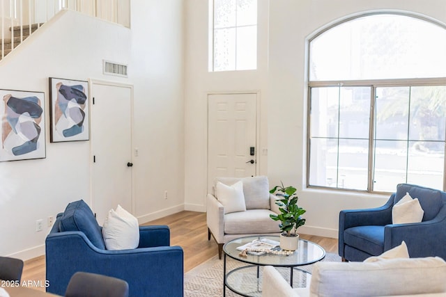 living area featuring light wood-style floors, baseboards, visible vents, and a high ceiling