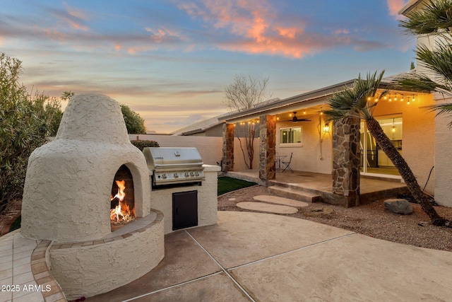 3037 E Bighorn Ave, Phoenix, AZ 85048 - patio terrace at dusk featuring a warm lit fireplace, exterior kitchen, grilling area, and fence