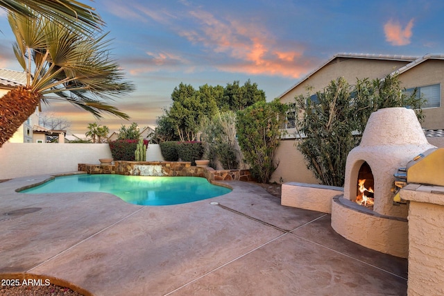 3037 E Bighorn Ave, Phoenix, AZ 85048 - pool at dusk with a patio area, a lit fireplace, a fenced in pool, and a fenced backyard