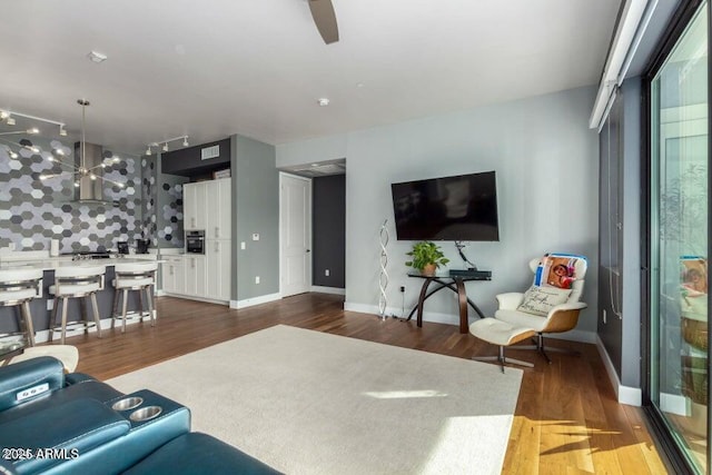 living room with dark wood-type flooring, ceiling fan with notable chandelier, and track lighting