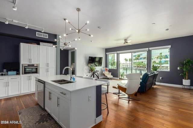 kitchen with pendant lighting, a kitchen island with sink, sink, and white cabinets