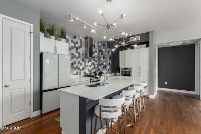 kitchen with sink, white refrigerator, a center island with sink, decorative light fixtures, and wall chimney exhaust hood