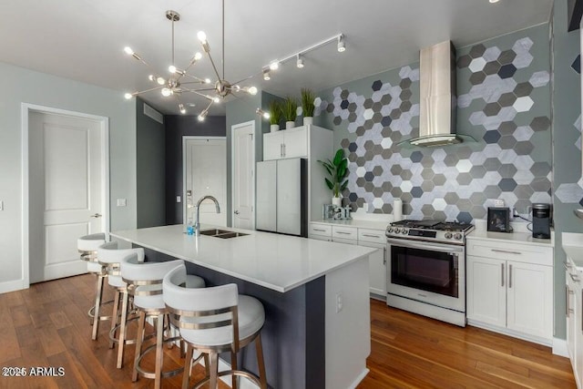 kitchen featuring appliances with stainless steel finishes, an island with sink, sink, a kitchen bar, and wall chimney exhaust hood