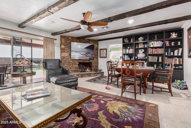 carpeted living room with beamed ceiling, a stone fireplace, and ceiling fan