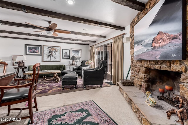 carpeted living room with beam ceiling, a stone fireplace, and ceiling fan