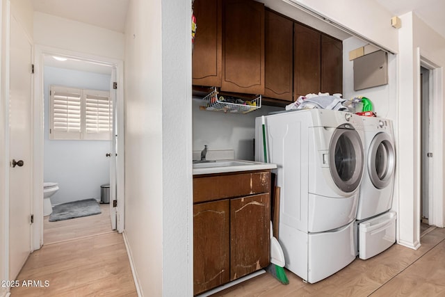 laundry room featuring cabinets, washer and dryer, sink, and light hardwood / wood-style flooring