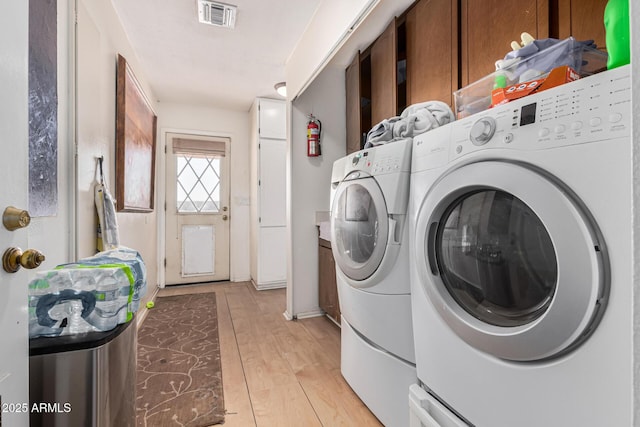 laundry room featuring washing machine and dryer, cabinets, and light wood-type flooring