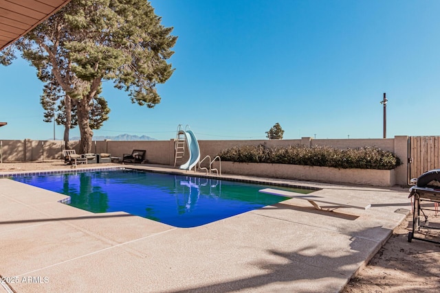 view of swimming pool with a water slide, a diving board, and a patio