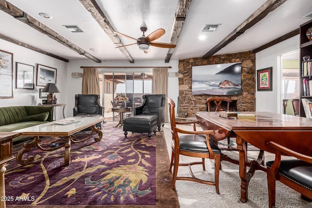 living room featuring beamed ceiling, ceiling fan, a stone fireplace, and carpet